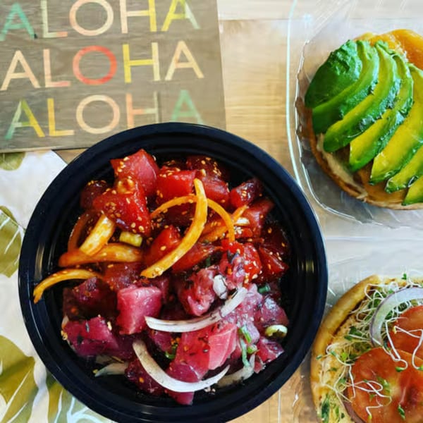 A poke bowl with tuna, onions, and sesame seeds, next to two avocado and tomato flatbreads.